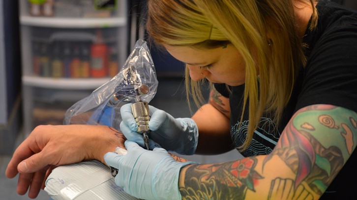 Tattoo artist Lacey Cormier creates a Polynesian pattern on Erik Wintner's right arm. 
