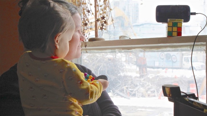 A mother and child look out their living room window at a construction site.