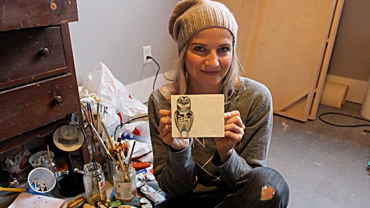 Woman holds painting next to paint brushes