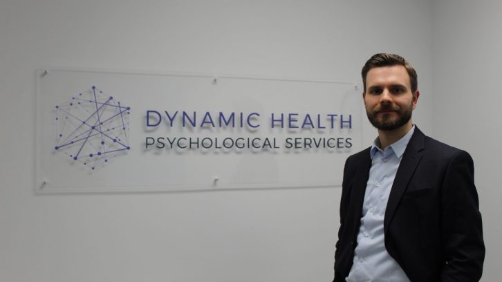 Dr. Joel Town stands in front of the sign for Dynamic Health Psychological Services