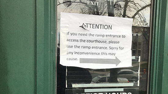 The paper sign displaying text and an arrow pointing right. It reads "If you need a ramp entrance to access the courthouse, please use the ramp entrance. Sorry for any inconvenience this may cause"