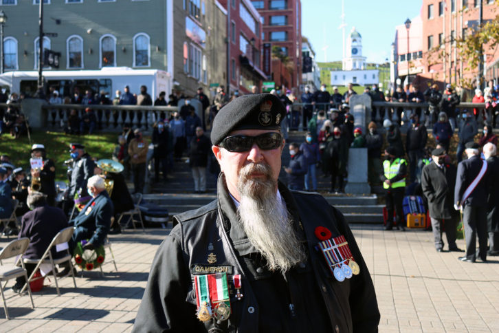 A man with a long beard and beret stands in crowd of people.