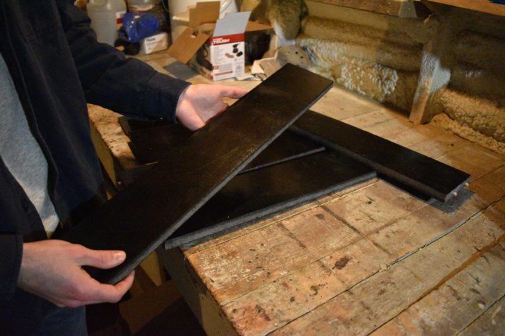 Cavanaugh holds a shiny black board. Other boards are piled up on a workbench.