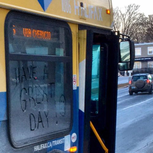 The side of a bus window, with the phrase ‘have a great day’ written in the frost. 
