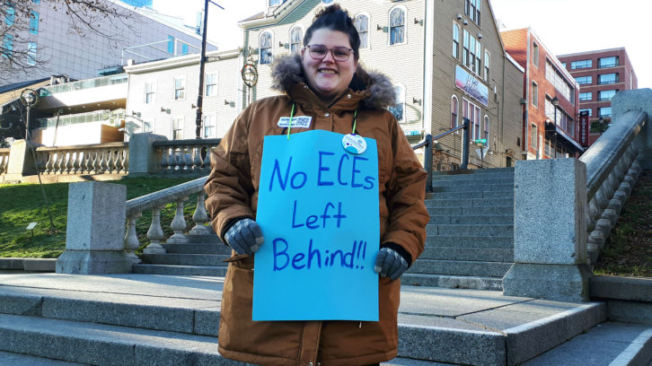 A woman holding a sign that says "No ECEs left behind!"