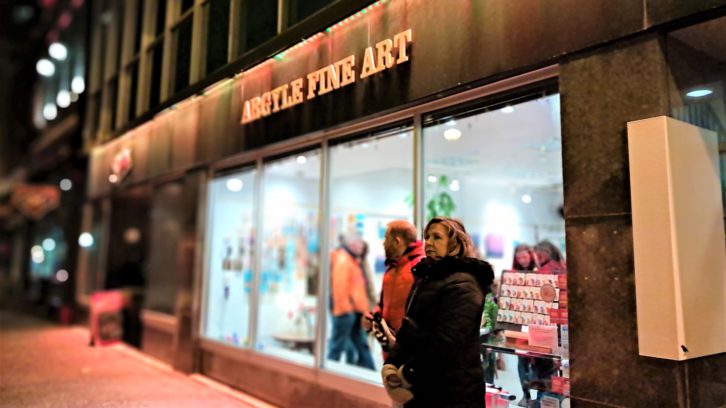 Two people stand in front of the window of a building that reads “Argyle Fine Art.”