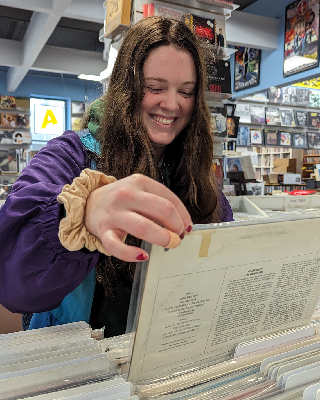 Jaime Hepditch flips through records at Taz Records on Grafton Street in Halifax. She's wearing a purple and blue jacket while smiling as she pulls up a record to read the album cover.