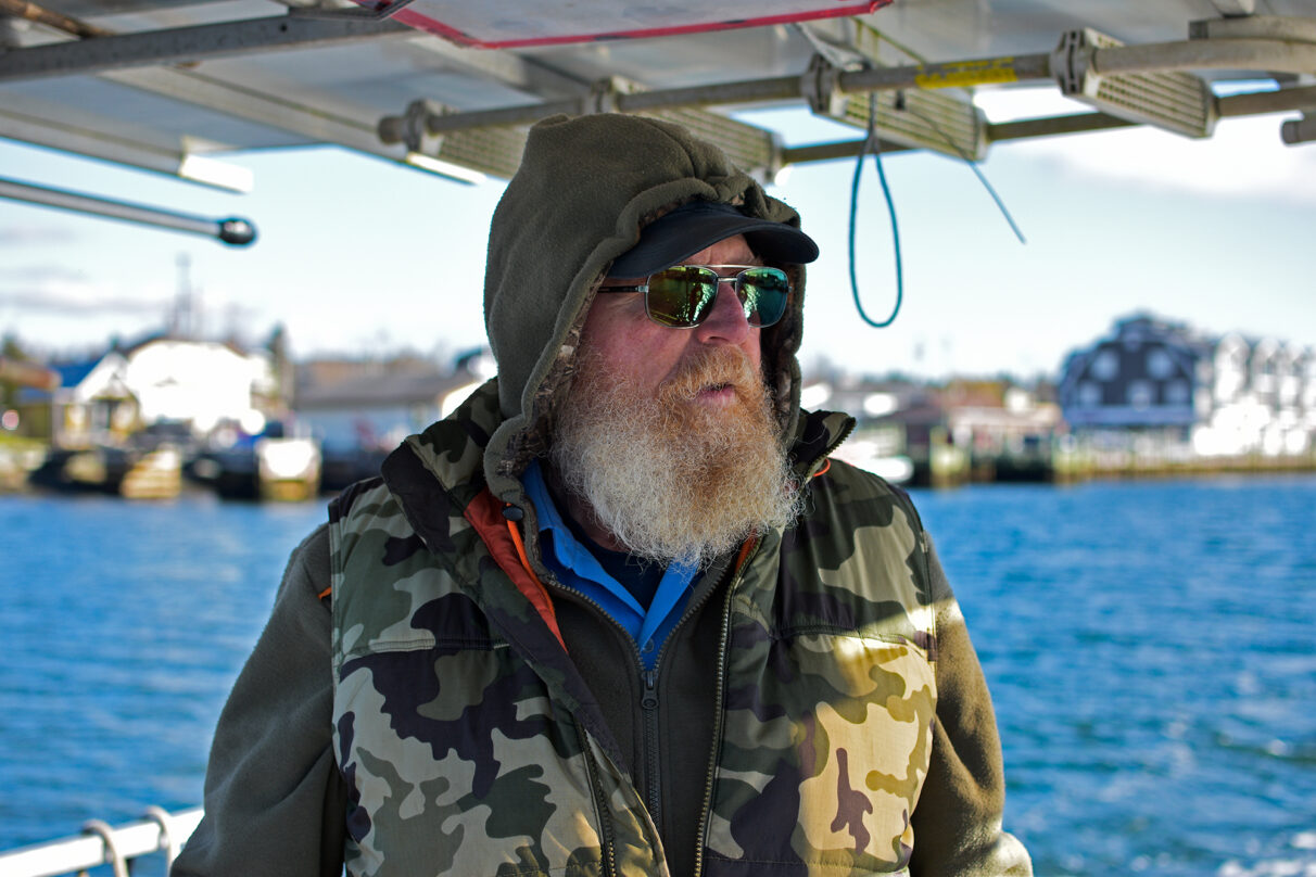 A bearded man stands on a ferry boat off the coast of Fishermans Cove in Halifax, Nova Scotia