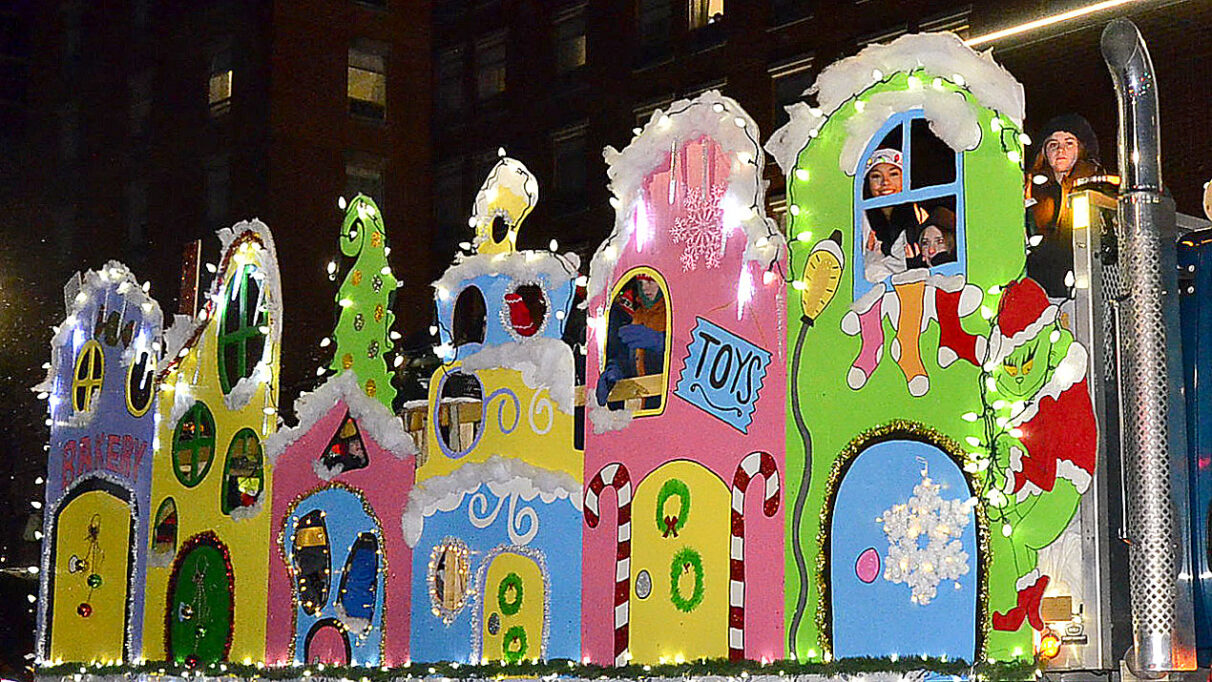 A parade float with six colourful houses featuring candy canes, snowflakes, bright lights and the Grinch.