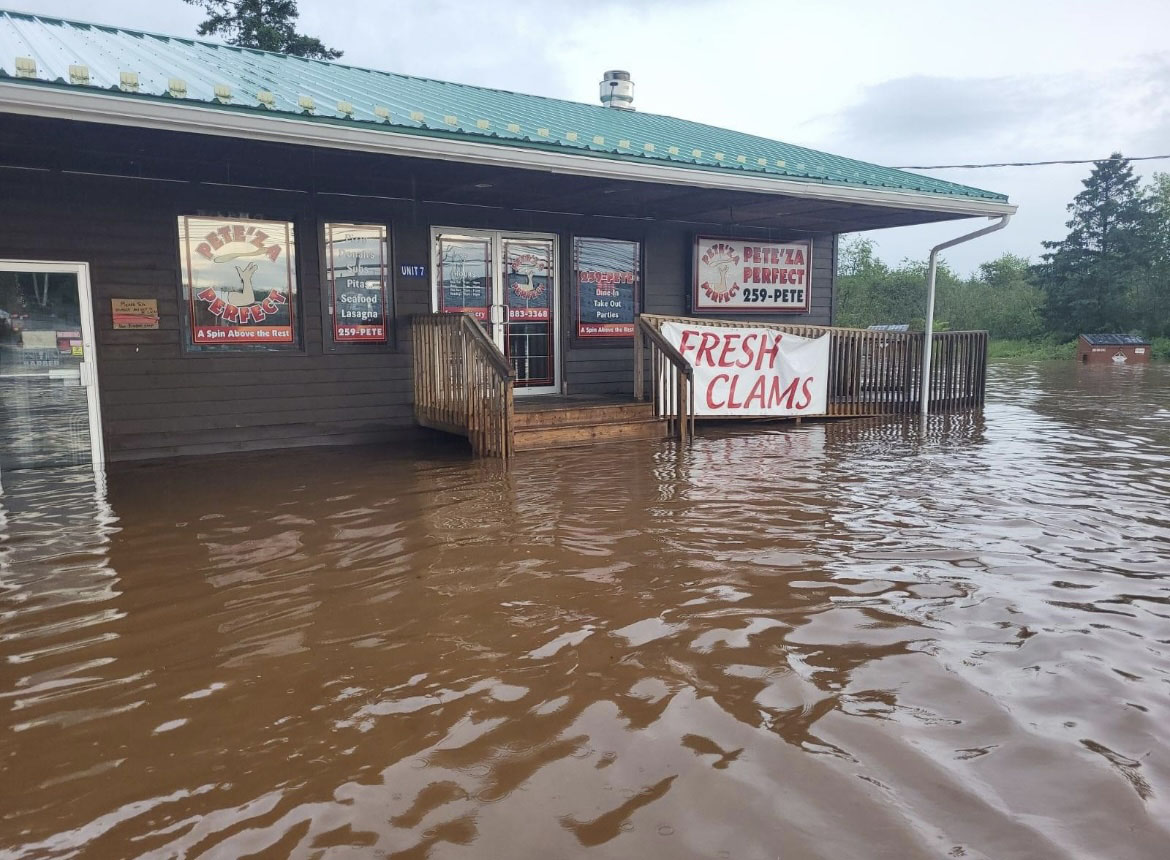 Flood water surrounds the exterior of pizza shop.
