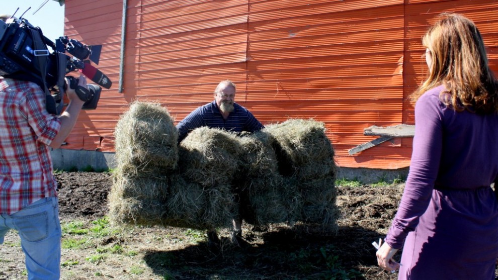 Colleen Jones and her cameraman watch a strongman lift eight hay bales at once.