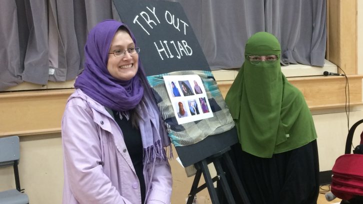 Alex Holmberg (left) tries on the hijab at Arazoo Hoseyni (right)'s table 