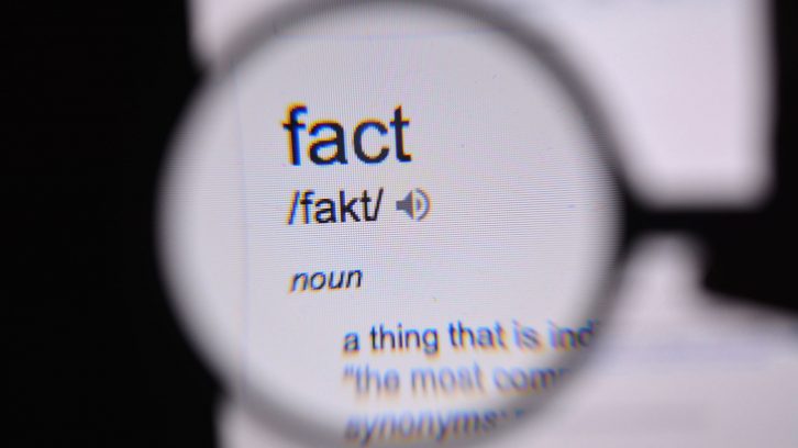 A person looks through a magnifying glass at the definition of the word fact.