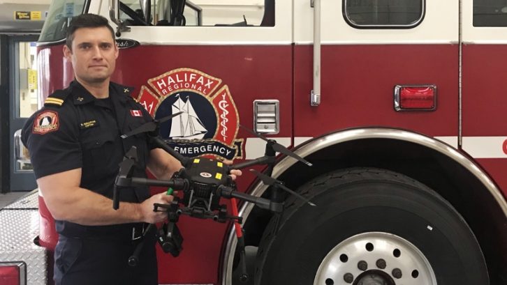 Captain Richard Sullivan stands in front of a Highfield Park fire truck holding the department's Matrice 210 drone. 