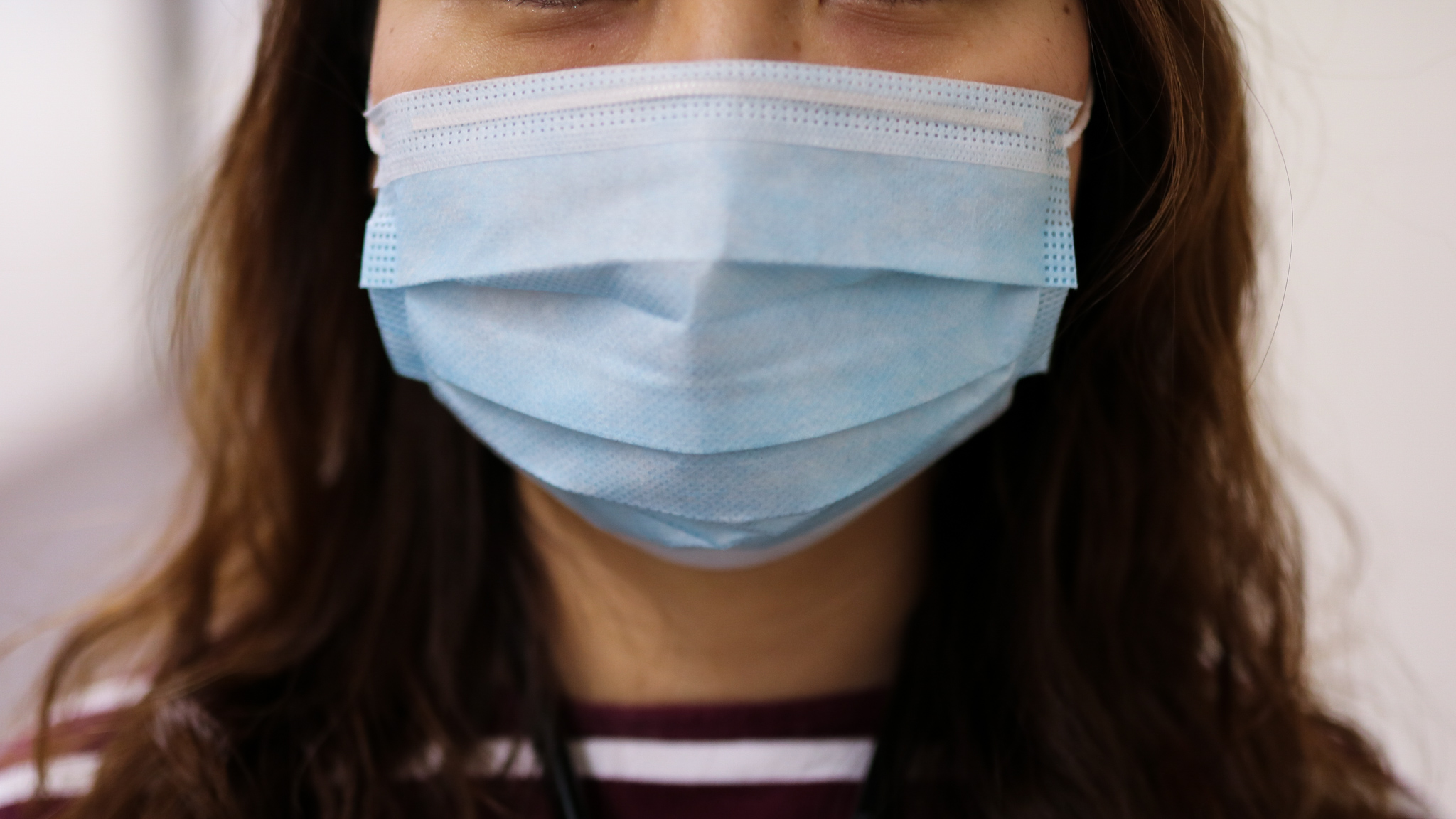 Photo illustration of a woman wearing a blue medical mask.