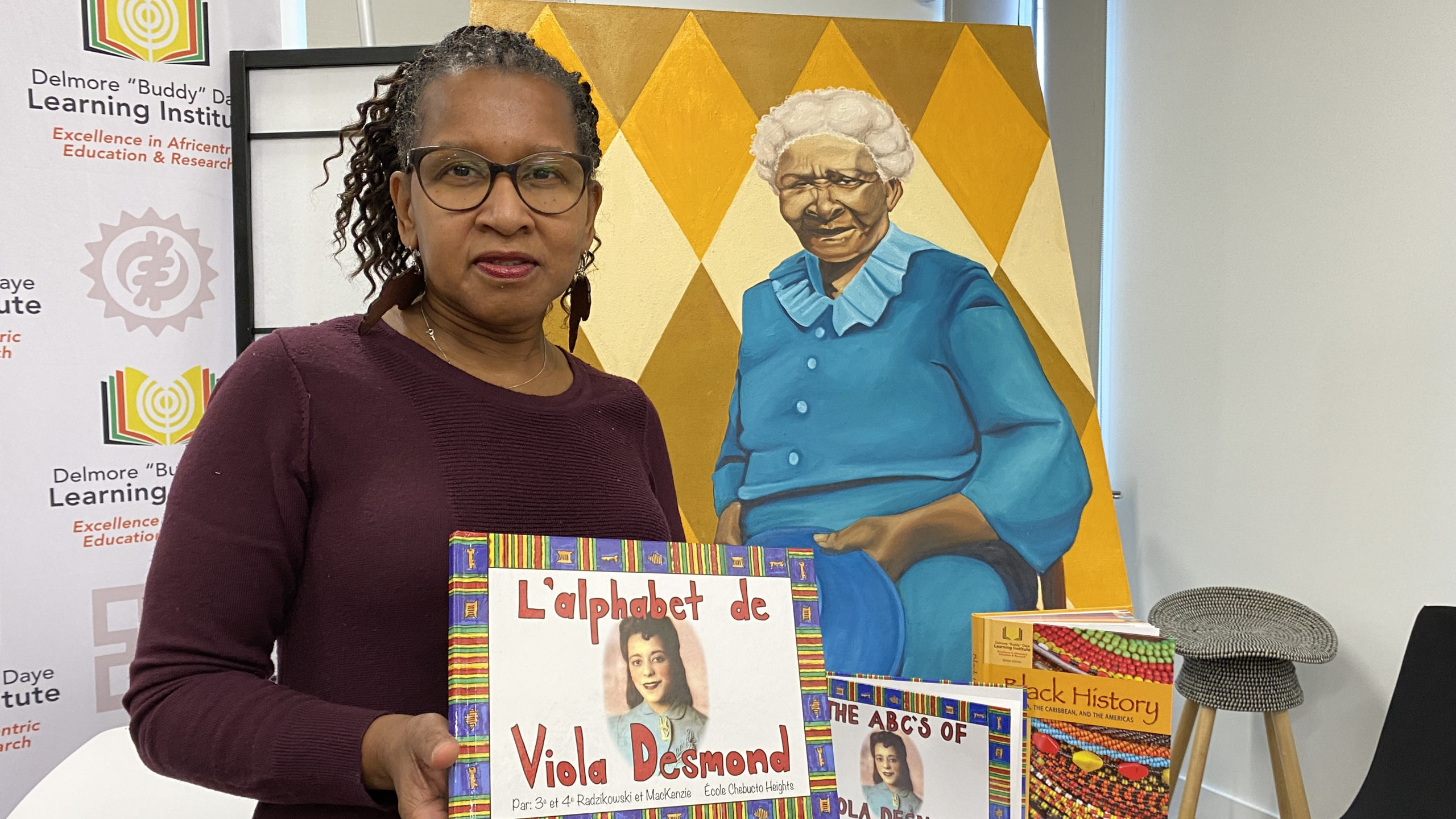 Sylvia Parris-Drummond poses with a selection of the Delmore "Buddy" Daye Learning Institute's educational materials and a painting by local artist Letitia Fraser that will be featured on the cover of a forthcoming textbook.