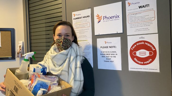 Melanie Sturk, director of organizational development for Phoenix Youth, poses outside her office with a box of cleaning supplies of the type being distributed to many of Phoenix's clients.