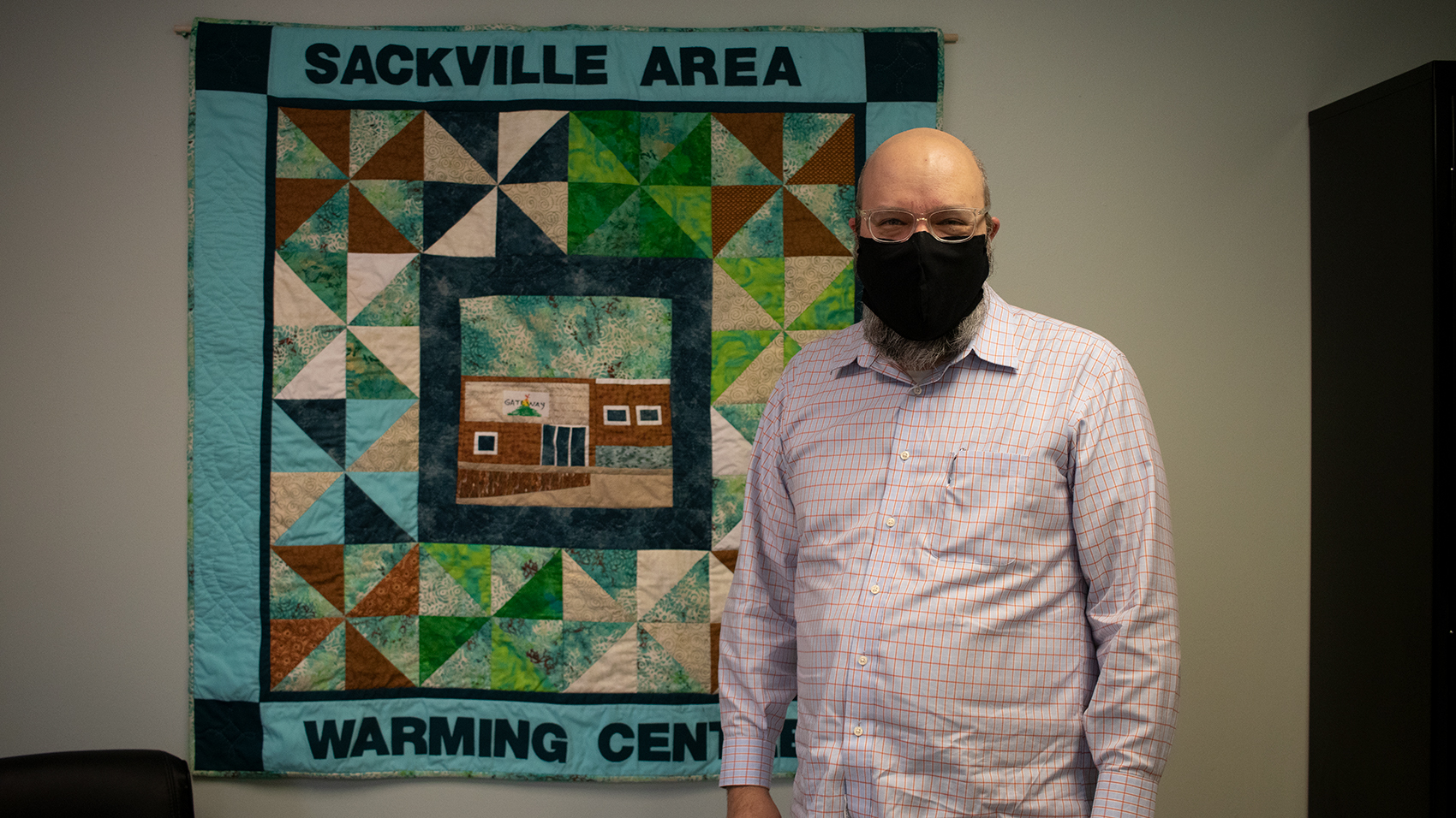 Mike Poworoznyk stands in front of a quilt inside the Sackville Area Warming Centre.