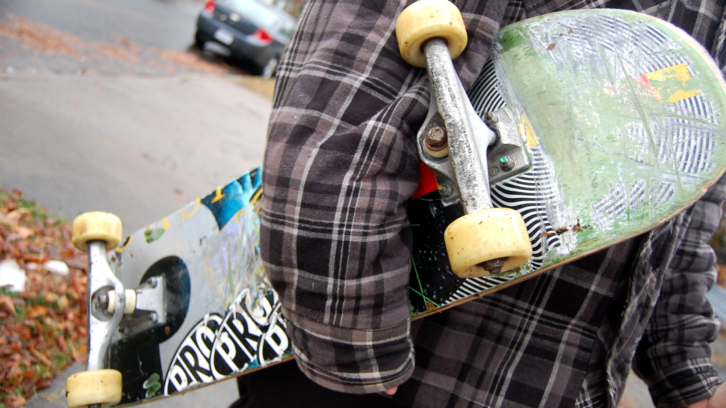 A person holding a skateboard under their arms.