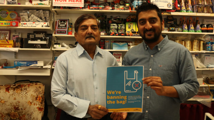 Krunal Shah and his dad pose with a government poster he says helped communicate the new rules to customers