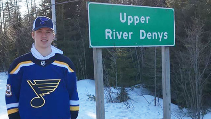 Recent NHL signee Colten Ellis stands next to his hometown sign of River Denys, in March 2020, while wearing his St. Louis Blues draft jersey. 