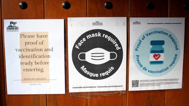 Reminders to wear masks and provide proof of vaccinations outside of the entrance at a Halifax pub. Police have charged 13 people in the Halifax area over the past week for not complying with public health orders.