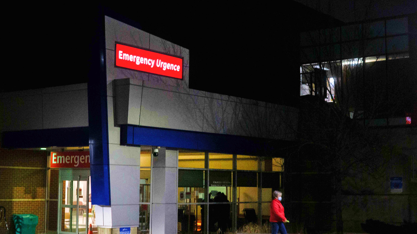 The entrance of the Halifax Infirmary emergency department is seen at night. A woman wearing a maxk walks away from the doors.
