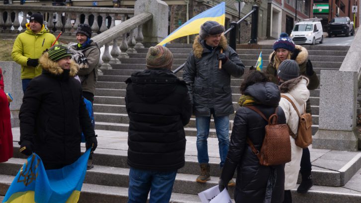 A man holding a Ukrainian flag stands on stone steps conversing with other people.