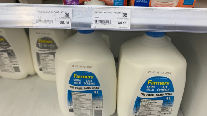 Milk is shown in a store refrigerator with the prices listed above.