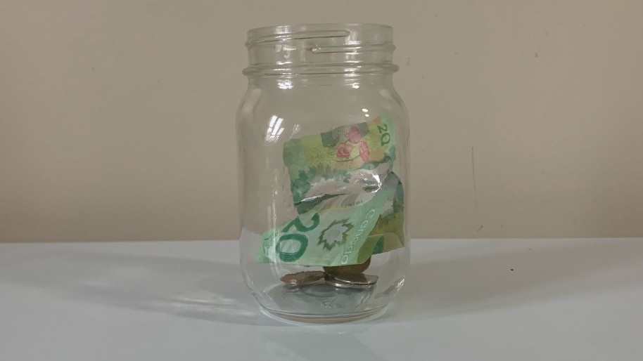 A mason jar is shown with a 20 dollar bill and loose change inside of it.