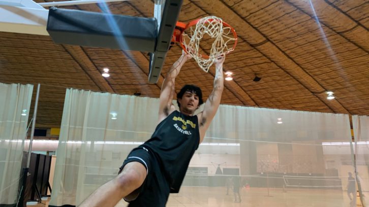A basketball player hangs from the rim inside of a basketball gym.