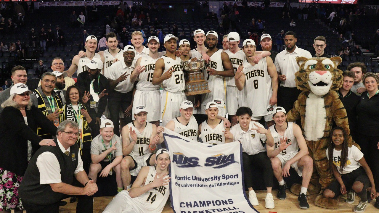 A basketball team poses together holding a trophy and a banner.