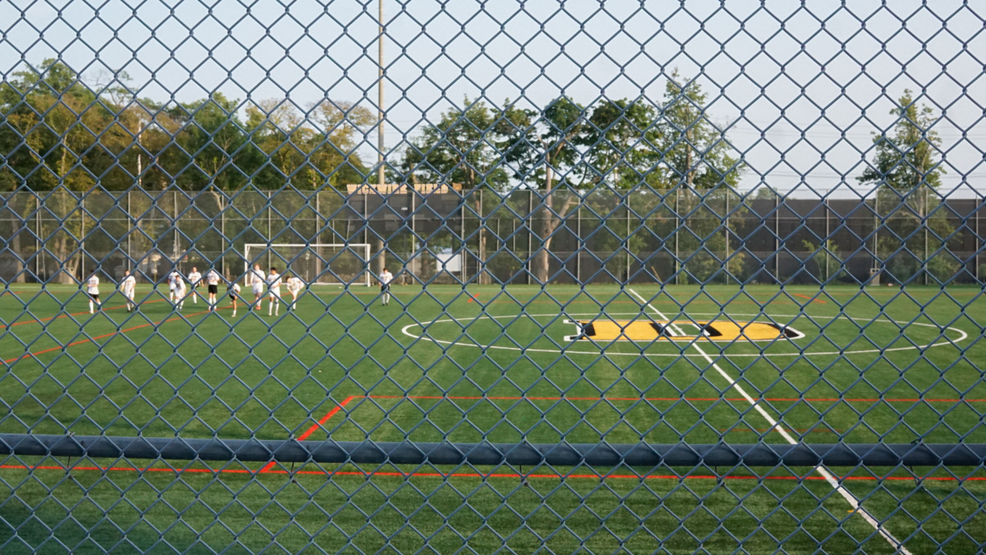 People are seen on a soccer field through a fence.