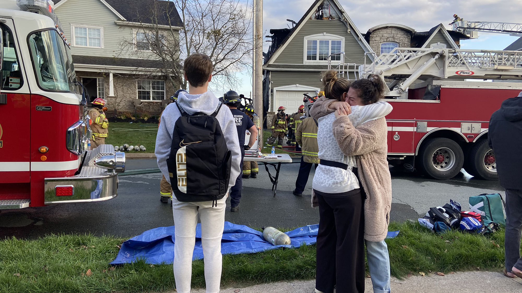 Women hug as fire crews work on a house damaged by fire