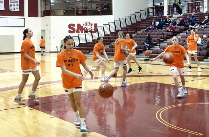 The SMU Huskies women's basketball team wearing orange shirts during warmup