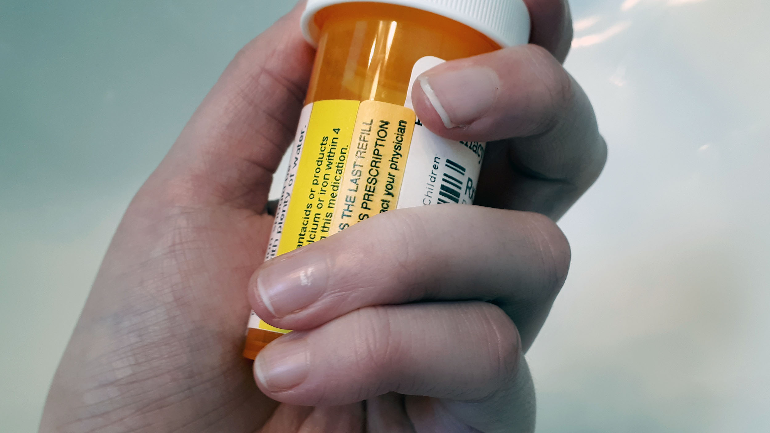 A hand holding a prescription bottle with a label asking the patient to contact their physician for a refill.