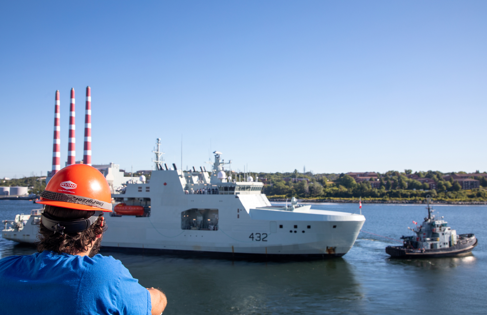 A shipyard worker looks out over Halifax Harbour as HMCS Max Bernays is guided by a tugboat. The Max Bernays is one of the navy's new Arctic patrol vessels being built at the Irving shipyard.