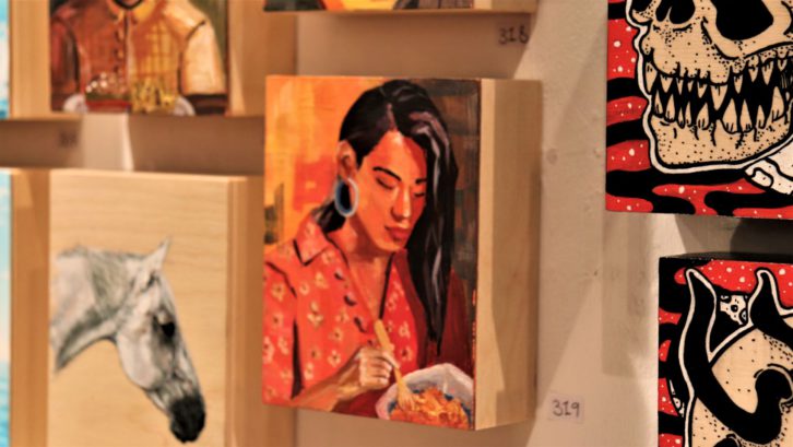 A painting of a horse and paintings of skeletons are next to a painting of a person with black hair and red clothing.