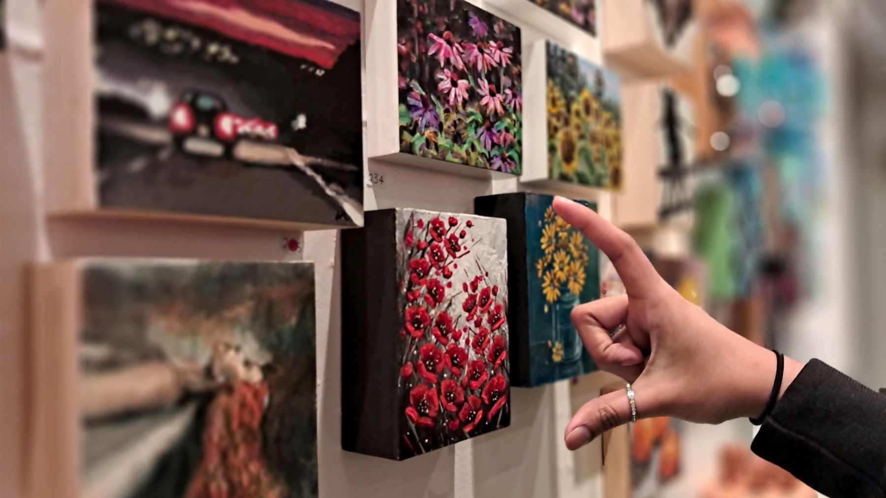 A person spreads their thumb and index finger in front of a painting of red flowers.