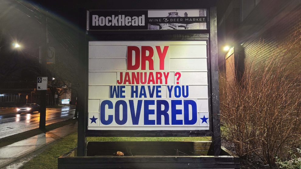 A large outdoor sign displays the text “Dry January? We have you covered.” It is nighttime and the sign is illuminated by surrounding streetlights.