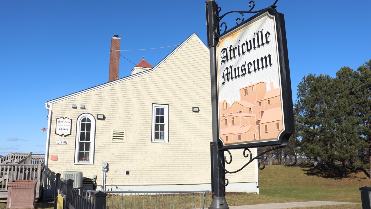 A sign reading “Africville Museum” sits in front of a cream-coloured church in a park.