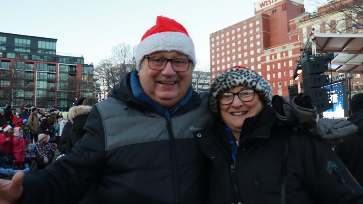 Couple wearing santa hats. A crowd of people is shown in the background.