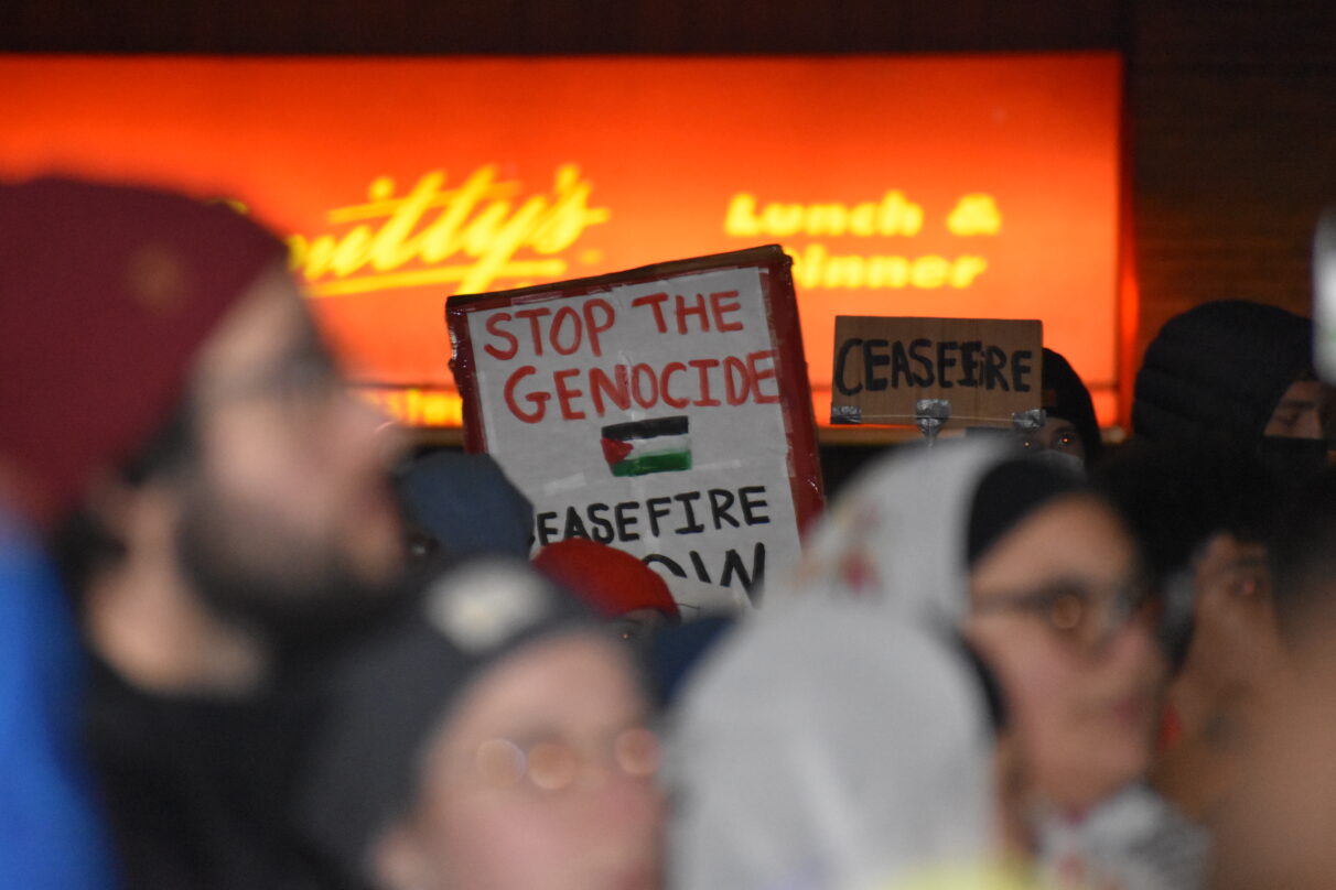 A sign focused in the center of the photo, with out of focused people in the foreground.