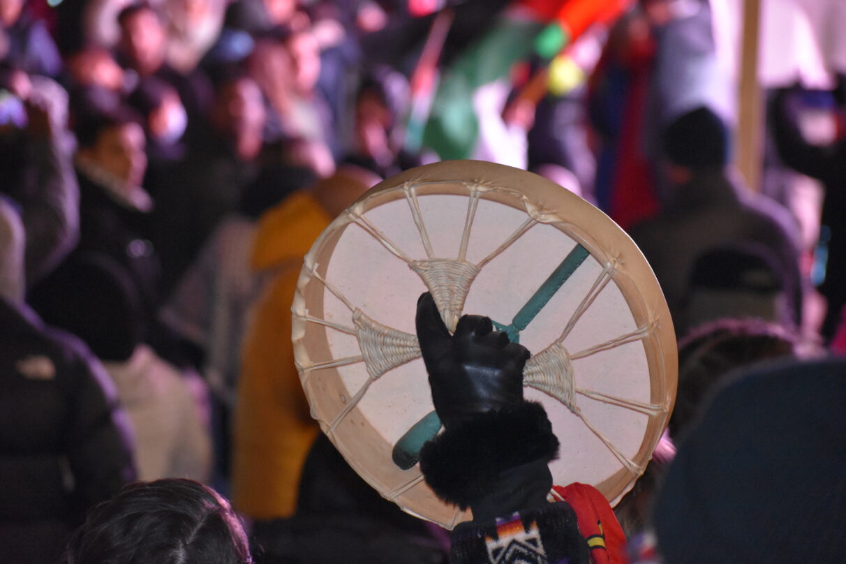 Out of focus background with the crowd, in the foreground a hand in focus holding a drum