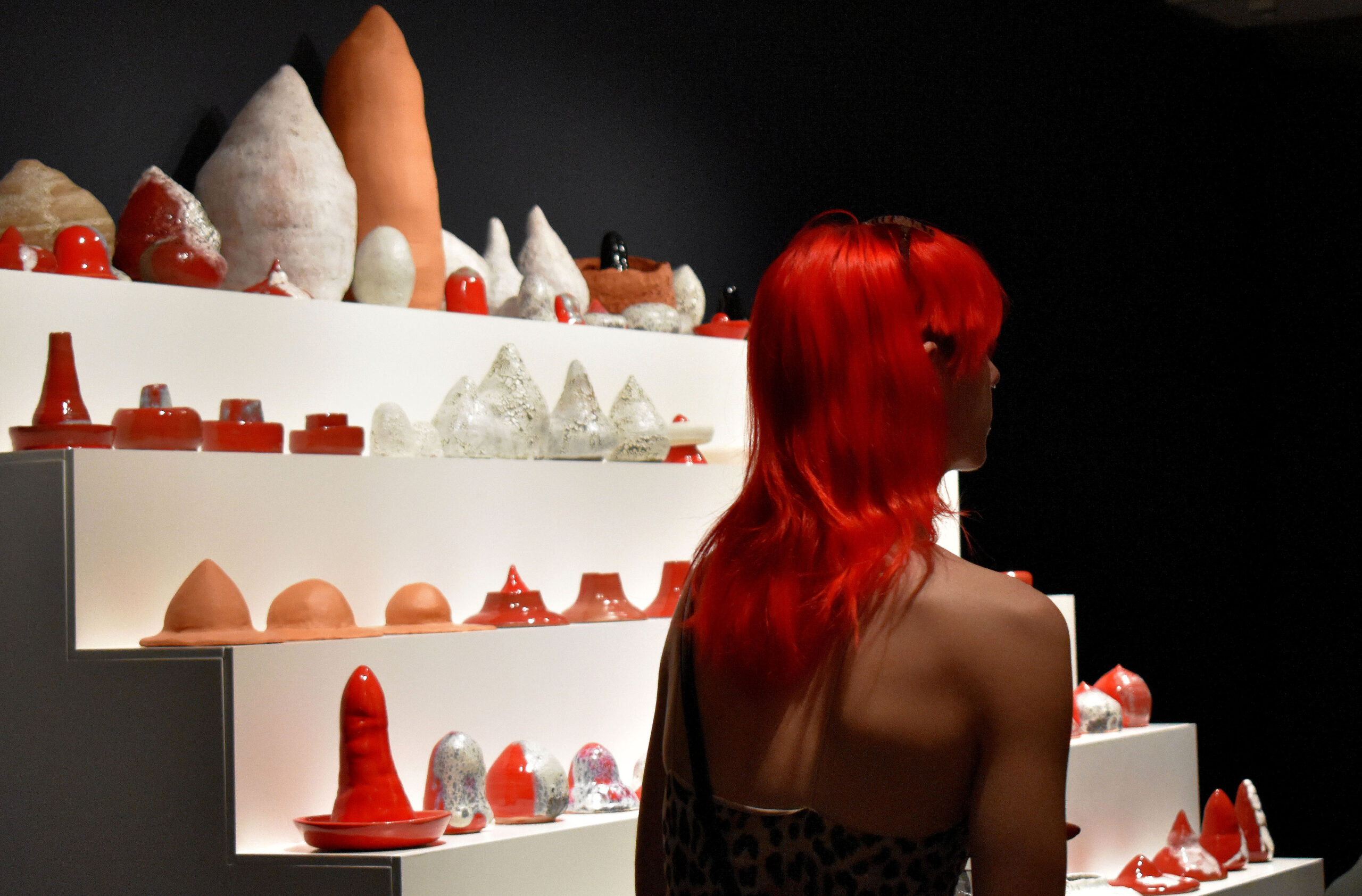 Woman with red hair stands in front of a display of objects