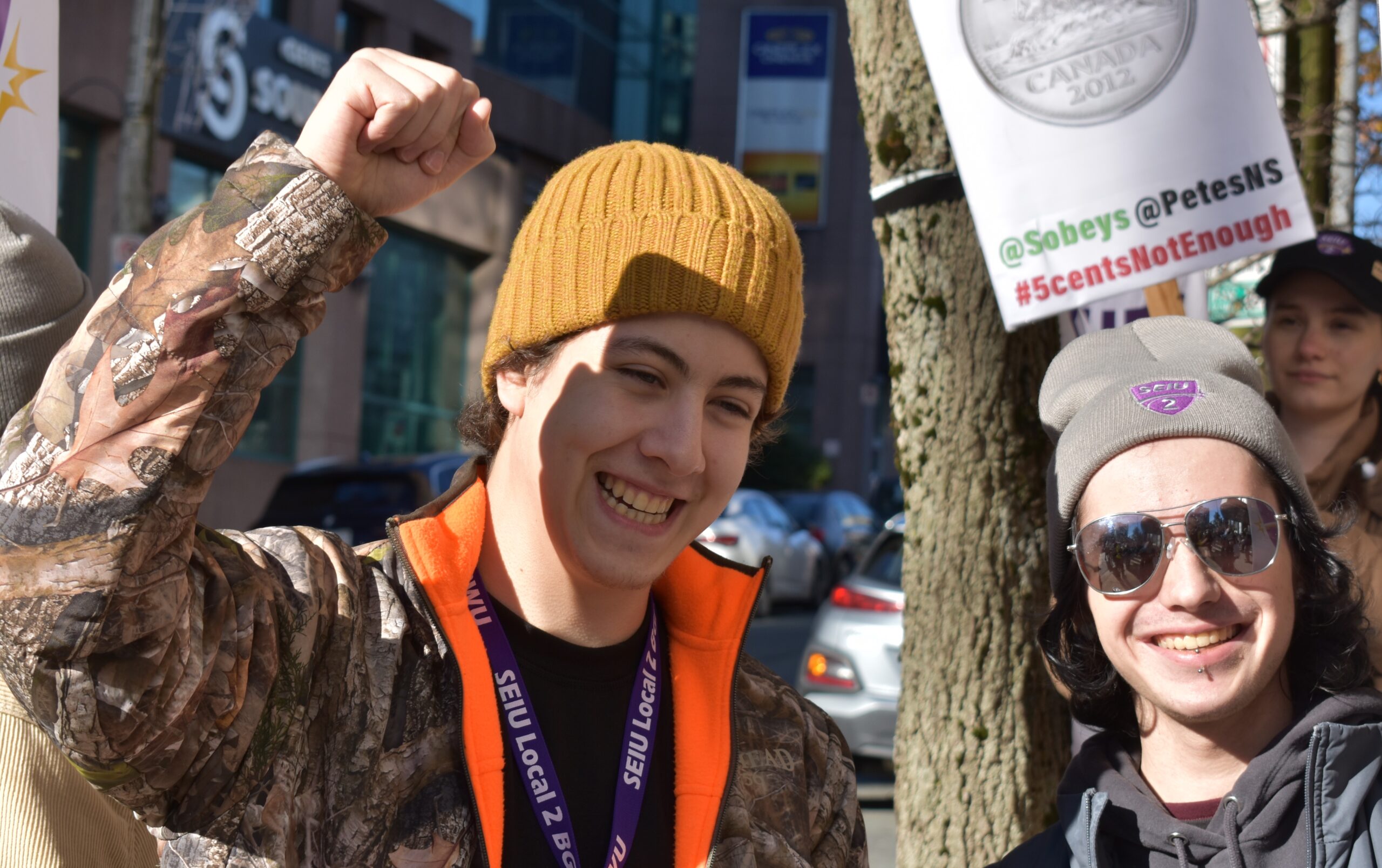 Person on the left has their fist in the air while smiling next to a person wearing a SIEU Local 2 hat on the left.