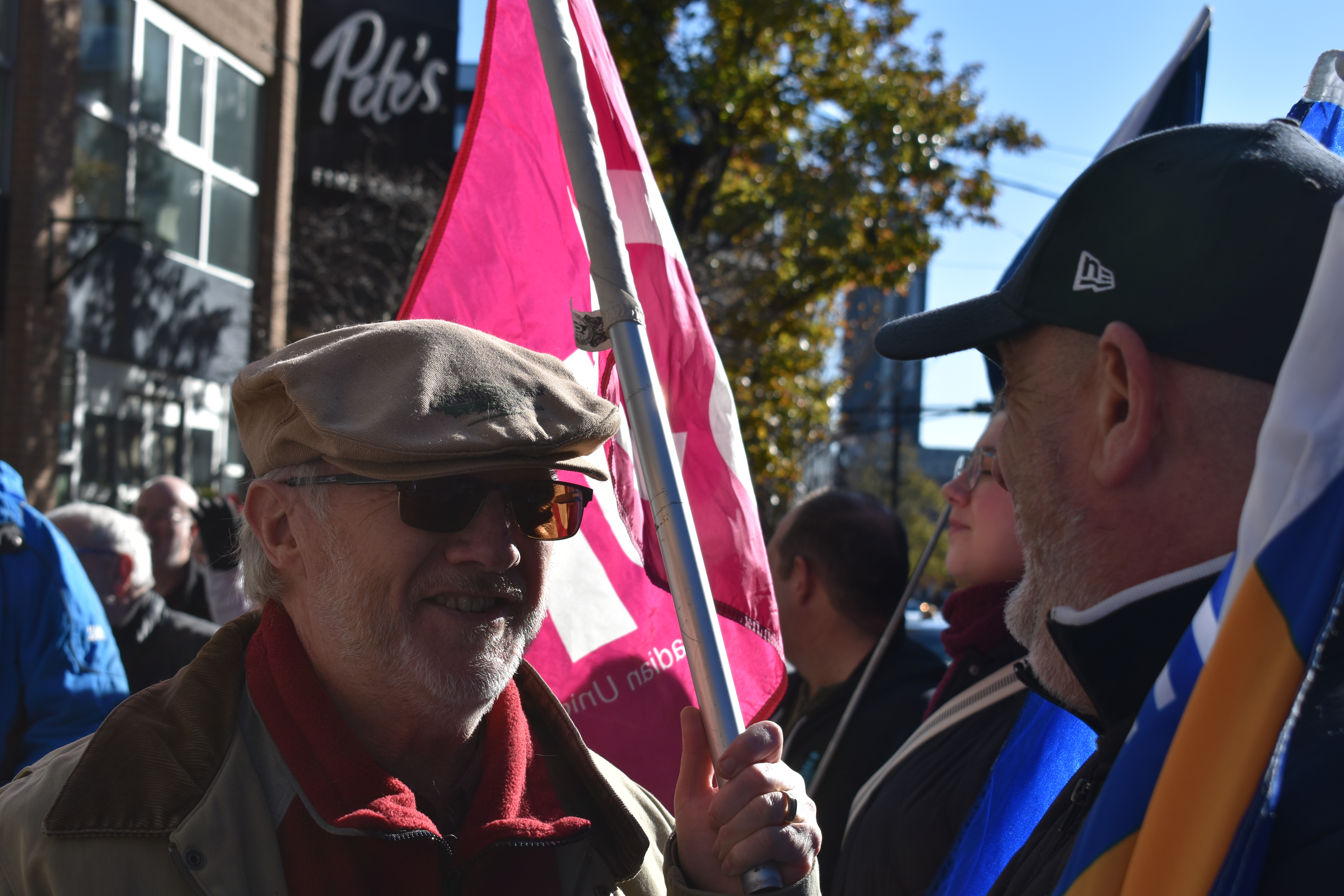 Two people are talking to each other. one on the left is holding a pink flag, while the one on the right is holding a blue and yellow flag.