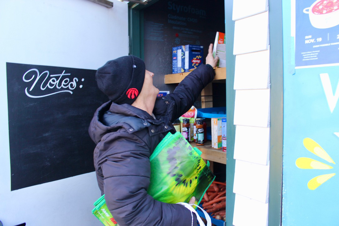 A woman is collecting food items in a pantry at an outside food bank.