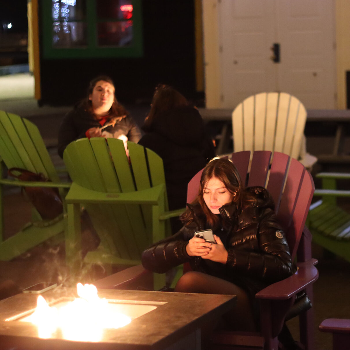 Girl sitting near a bonfire table looking at her phone.