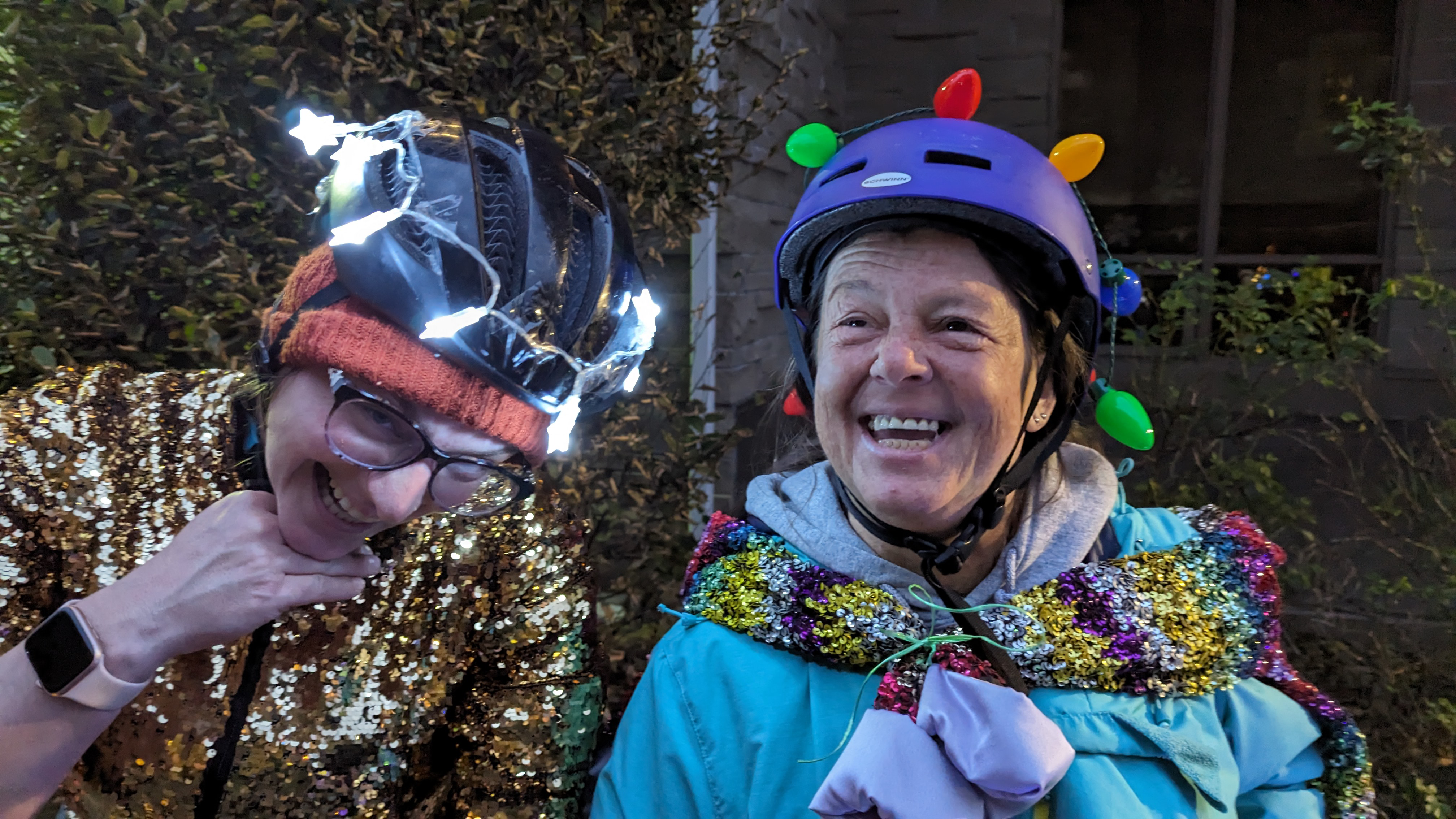 Shoulder shot of two smiling women dressed in bright flashy colours wearing helmets lit up with lights.